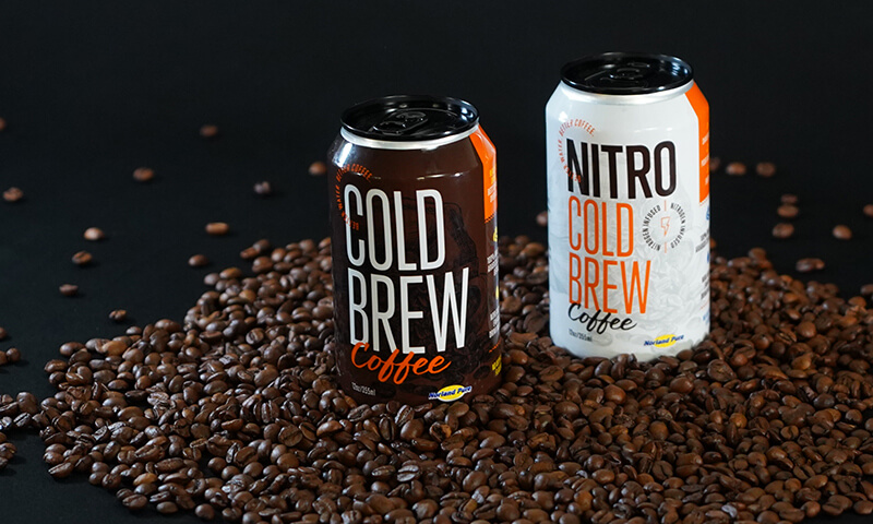 Two cans of cold brew coffee sitting in a pile of coffee beans